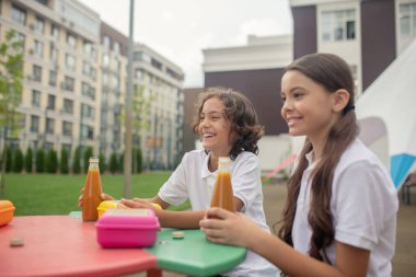 Arkadaşlar masada oturuyor ve birlikte yemek yiyorlar.