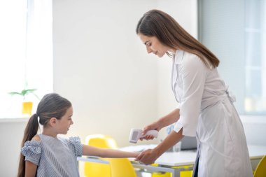 Koyu saçlı doktor, küçük hastasının ateşini ölçüyor.