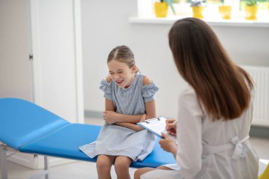 Karın ağrısı çeken ve doktorla konuşan bir kız.