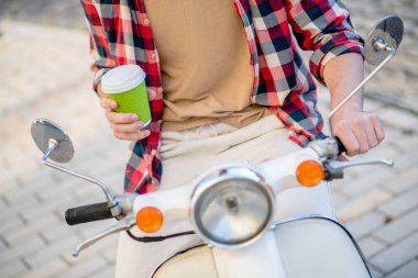 Scooter sürerken kahve içen bir adam.