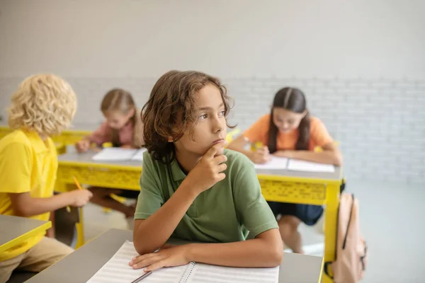 Egy fiú ül az asztalnál az osztályteremben és gondolkodik. — Stock Fotó