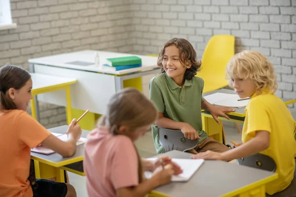 Děti sedí u psacích stolů ve třídě a vypadají spokojeně — Stock fotografie