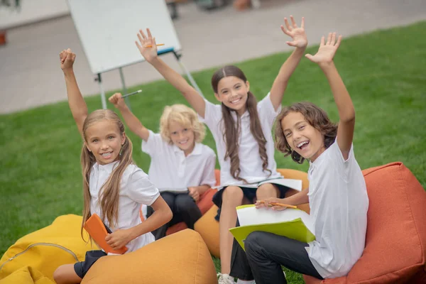 Grupo de alumnos sentados en bolsas de silla y levantando las manos — Foto de Stock