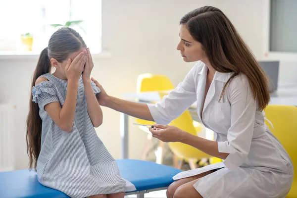 Niña mirando la jeringa en la mano de los médicos y sintiéndose asustada — Foto de Stock