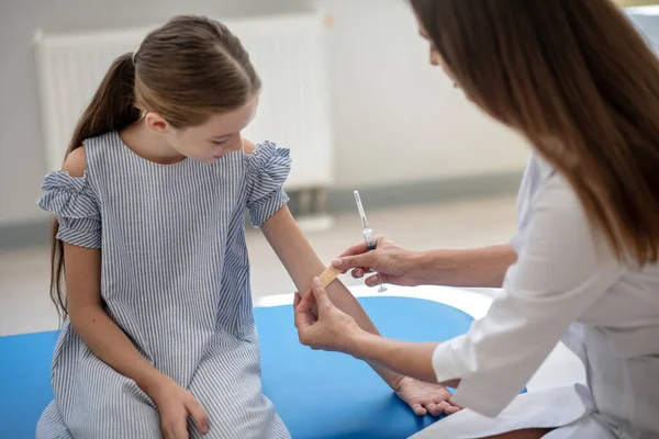 Läkare håller flickor arm och applicera ett plåster — Stockfoto