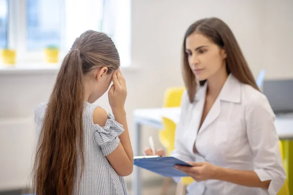 Menina com dor de cabeça e conversando com o médico — Fotografia de Stock