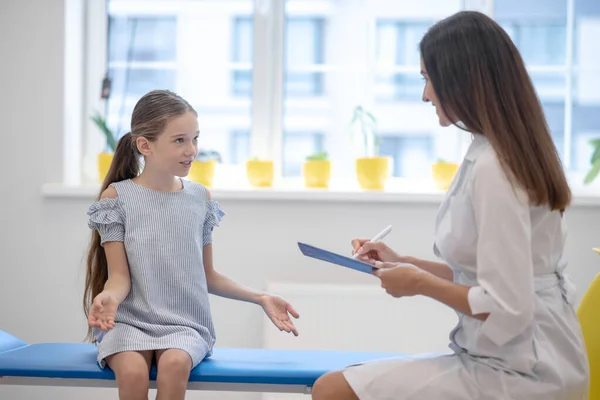 Κορίτσι με μπλε φόρεμα μιλάει με τη γυναίκα γιατρό και εξηγεί τα συμπτώματα — Φωτογραφία Αρχείου
