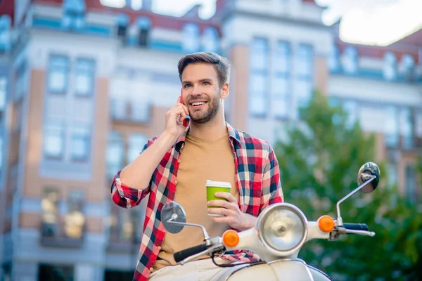 Pewny siebie mężczyzna rozmawiający przez telefon i siedzący na skuterze — Zdjęcie stockowe