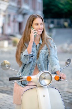 Scooter süren ve telefonda konuşan bir kadın.