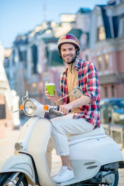 Улыбчивый мужчина за чашкой кофе во время езды на скутере — стоковое фото