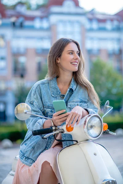 Donna seduta su uno scooter e utilizzando il suo smartphone — Foto Stock