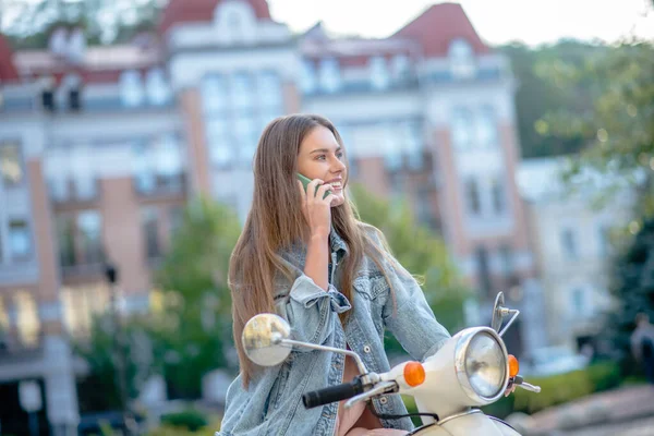 Mujer montando scooter y haciendo una llamada telefónica — Foto de Stock
