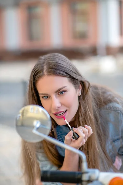 Woman using a lipstick while riding a scooter — Stock Photo, Image