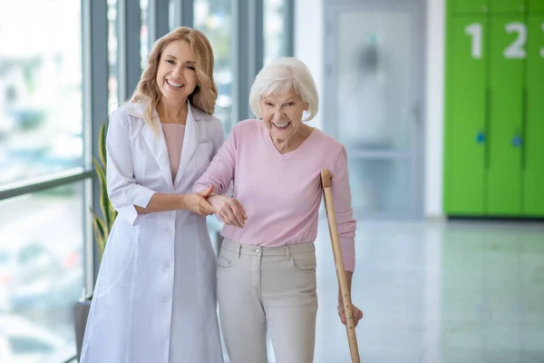 Smiling doctor in a lab coat walking with a senior patient