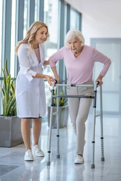 Laboratuvar önlüklü bir kadın doktor. Yanında Rolling-walker 'ı olan yaşlı bir hasta var. — Stok fotoğraf