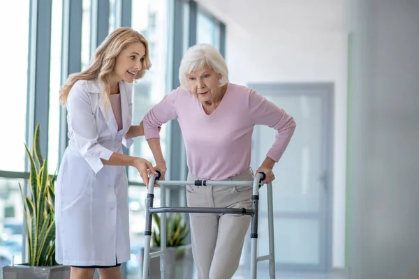 Vrouwelijke arts in een laboratoriumjas moedigt een senior patiënt met rollator — Stockfoto