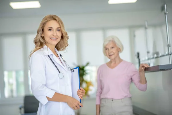 Blond lächelnder Arzt steht in der Nähe seiner Patientin in der Klinik — Stockfoto