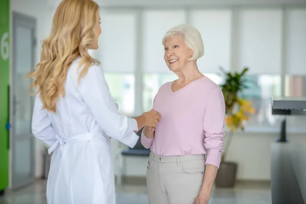 Старша жінка розмовляє з лікарем в клінічному коридорі і тримає руку — стокове фото