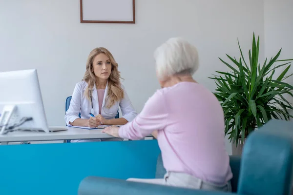 Blonde doctor sitting at the table and listening to the patient carefully