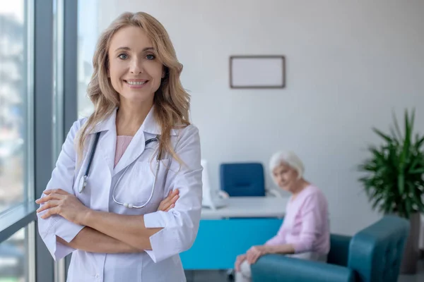 Långhårig blond läkare står med armarna korsade och ler — Stockfoto