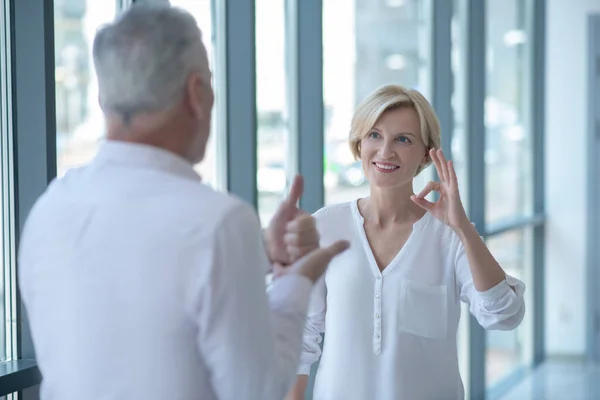 Wesoła blondynka rozmawia z siwym mężczyzną używając języka migowego — Zdjęcie stockowe