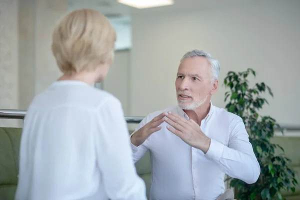 Vousatý šedovlasý muž a blondýna mluví znakovou řečí — Stock fotografie