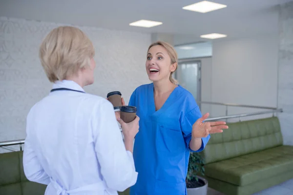 Two female doctors drinking coffee, laughing, talking