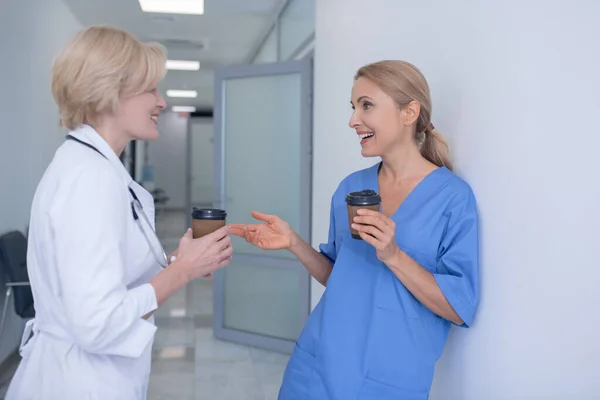 Två leende kvinnliga läkare står i korridoren, dricker kaffe — Stockfoto