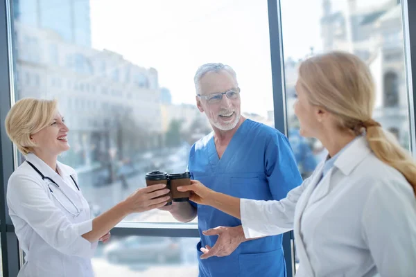 Smiling medical workers drinking coffee, having friendly conversation