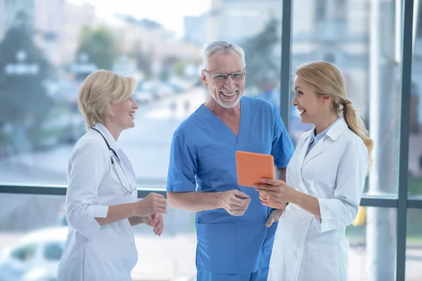 Médicos sonrientes estudiando algo en la tableta, teniendo una conversación amistosa — Foto de Stock