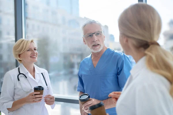 Uśmiechnięta drużyna szpitalna pije kawę, prowadzi przyjazną rozmowę — Zdjęcie stockowe