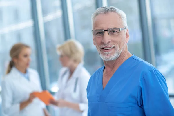 Männlicher Arzt lächelt in die Kamera, seine Kolleginnen stehen mit Tablette dahinter — Stockfoto