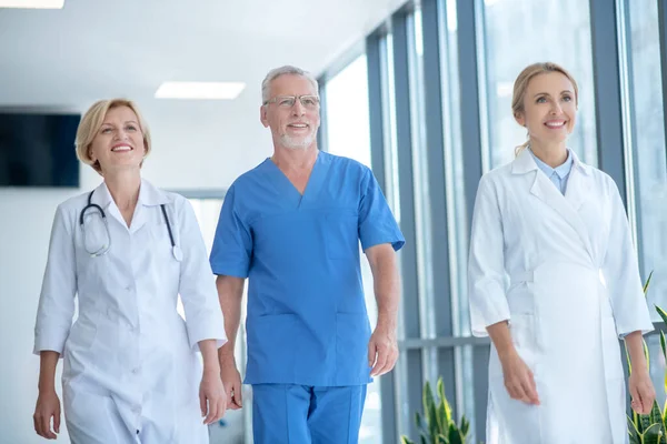 Группа улыбающихся медицинских работников, идущих по коридору больницы — стоковое фото