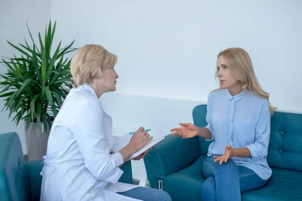 Paziente femminile seduta sul divano, consulta il medico femminile bionda matura — Foto Stock