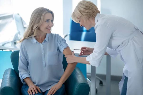 Blonde femme médecin faire injection dans le bras de sourire patiente — Photo