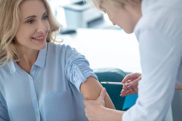 Žena lékař dělat injekce do ramene blond pacientky — Stock fotografie