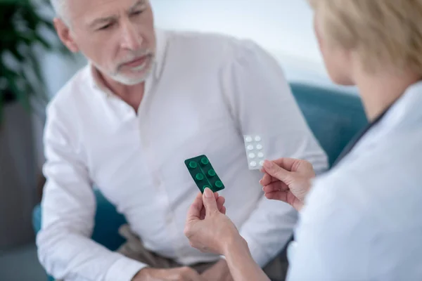 Female doctor giving two blister packs with pills to gray-haired male patient