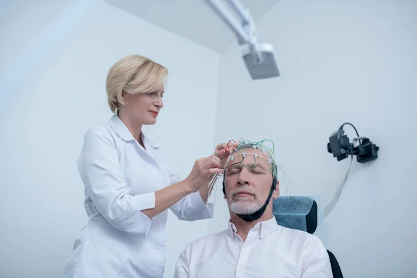 Női neurológus helyezi elektróda sapka ősz hajú férfi beteg fejét — Stock Fotó
