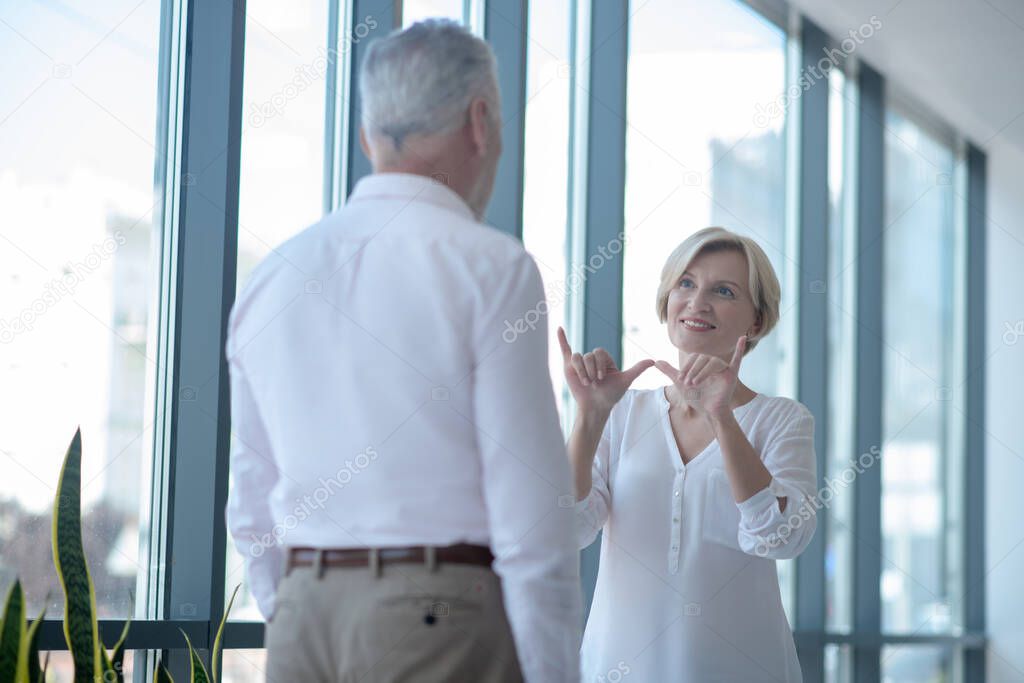 Smiling blonde female talking with gray-haired male using sign language