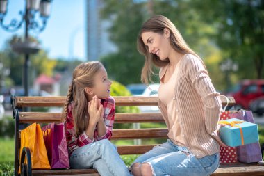 Gülümseyen anne, sürpriz kızını parktaki bankta sunar.