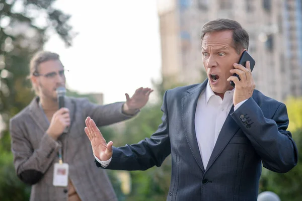 Mature man speaking on the phone, pushing male journalist away — Stock Photo, Image