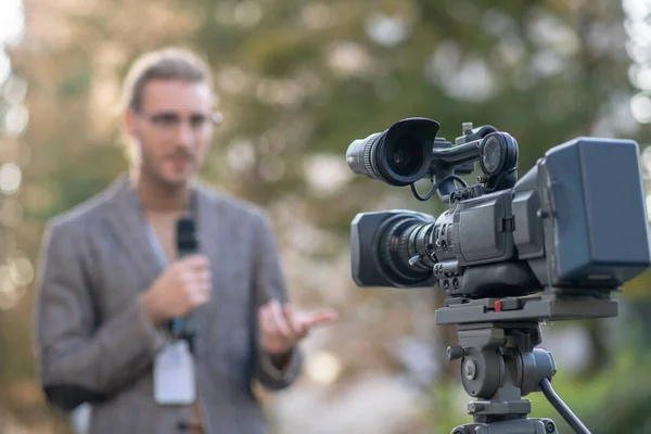 Un reportero de cabello rubio hablando en el micrófono frente a la cámara afuera —  Fotos de Stock