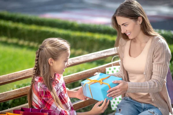 Sorrindo mãe dando sua filha caixa de presente no banco do parque — Fotografia de Stock