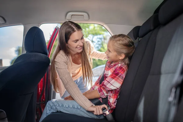 Gülümseyen anne, kızının emniyet kemerini arabanın arka koltuğuna bağlıyor. — Stok fotoğraf