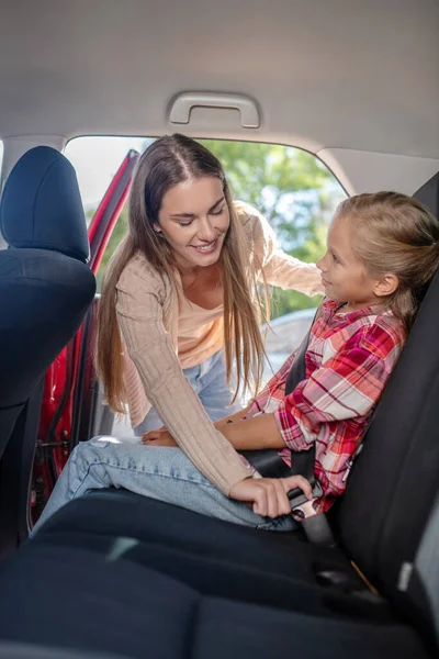 Önemseyen anne, kızının emniyet kemerini arabanın arka koltuğuna bağlıyor. — Stok fotoğraf
