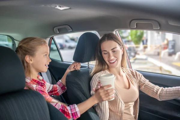 Menina dando xícara de café para sua mãe sentada ao volante — Fotografia de Stock