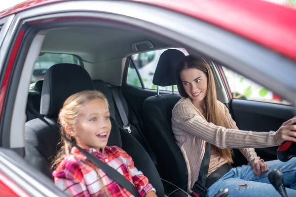 Smiling mom driving with her lovely girl sitting on passenger seat — Stock Photo, Image