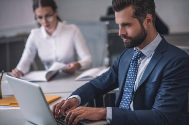 Bilgisayarda çalışan bir iş adamı, uzakta oturan bir kadın.