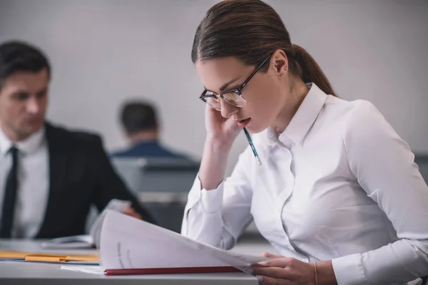 Jeune femme adulte à lunettes lisant attentivement les documents — Photo