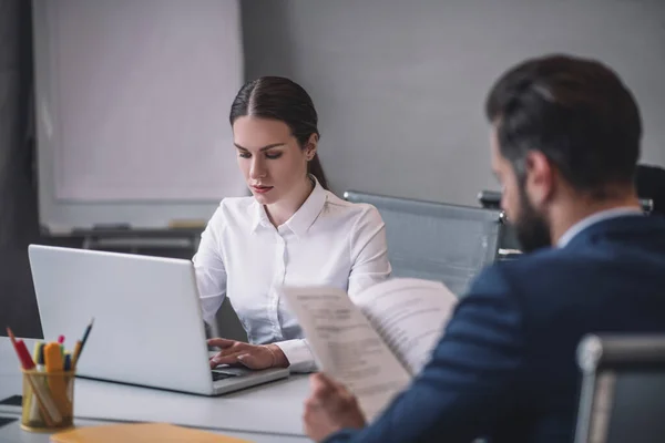 Pretty woman behind laptop and man reading opposite — Stock Photo, Image